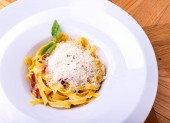 Klasické těstoviny Carbonara, špagety s pancetta, slaninou, vajíčkem, parmazánem a zelenou arugulkou na dřevěném stole.