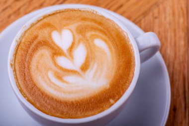 Latte sıcak kahve veya kapuçino ahşap masa arka plan üzerinde latte sanat ile beyaz bir fincan.