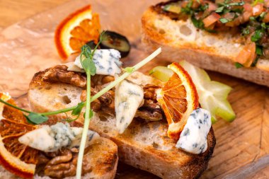 Ahşap masa üzerinde peynir, bal, ceviz ve kuru portakal dilimleri ile meze bruschetta. Makro.