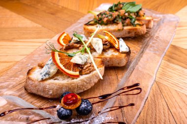 Ahşap masa üzerinde peynir, bal, ceviz ve kuru portakal dilimleri ile meze bruschetta. Close.