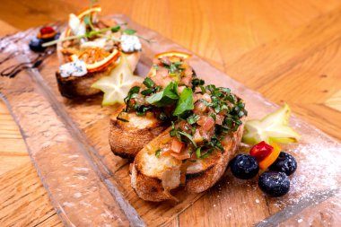 Lezzetli tuzlu domates İtalyan mezeler, veya bruschetta, fesleğen ile süslenmiş tost baget dilimleri üzerinde, ahşap bir masaya yakın.