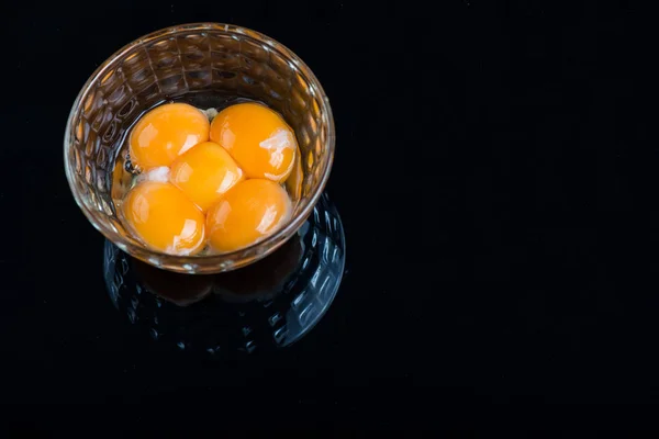 Bright yellow egg yolks in a glass bowl on black background