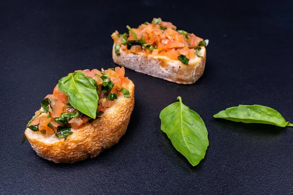 おいしい風味のトマトイタリアン前菜、またはブルスケッタ、バジルとアボカドで飾られたトーストバゲットのスライスに — ストック写真