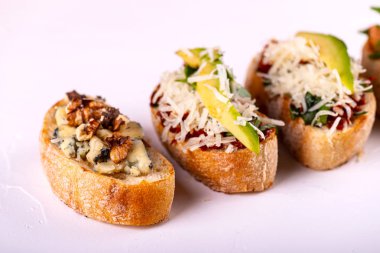 Brushetta bir aperatif için ayarlayın. Beyaz arka planda domates, parmesan peyniri, avokado ve ceviz ile küçük sandviç çeşitleri