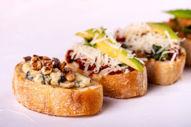 Brushetta bir aperatif için ayarlayın. Beyaz arka planda domates, parmesan peyniri, avokado ve ceviz ile küçük sandviç çeşitleri