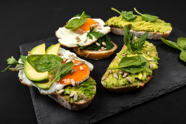 Sandwiches with avocado, spinach and fried eggs on a black background