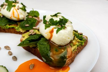 Avokado ile haşlanmış yumurta, ıspanak yaprakları ve beyaz arka plan üzerinde beyaz bir tabak üzerinde tost ekmek üzerinde tohum. Sağlıklı kahvaltı veya atıştırmalık. Close