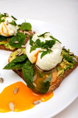 Avokado ile haşlanmış yumurta, ıspanak yaprakları ve beyaz arka plan üzerinde beyaz bir tabak üzerinde tost ekmek üzerinde tohum. Sağlıklı kahvaltı veya atıştırmalık. Close.