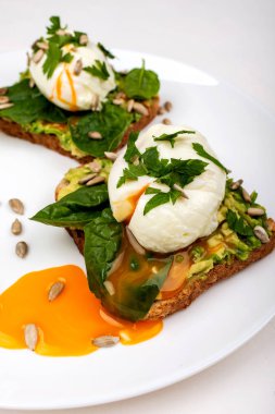 Avokado ile haşlanmış yumurta, ıspanak yaprakları ve beyaz arka plan üzerinde beyaz bir tabak üzerinde tost ekmek üzerinde tohum. Sağlıklı kahvaltı veya atıştırmalık.