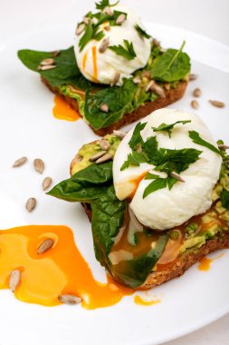 Avokado ile haşlanmış yumurta, ıspanak yaprakları ve beyaz arka plan üzerinde beyaz bir tabak üzerinde tost ekmek üzerinde tohum. Sağlıklı kahvaltı veya atıştırmalık.