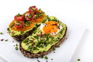 Avokado guacomole, yumurta ve domates, yeşil pırasa ve susam ile Sandviçler. Beyaz arka planda sağlıklı kahvaltı veya atıştırmalık.