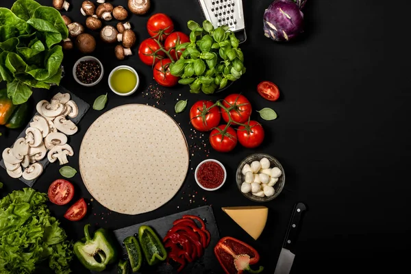 Samenstelling met pizza deeg en rauwe ingrediënten voor het koken van Italiaanse pizza. Bovenaanzicht op een zwarte achtergrond. — Stockfoto