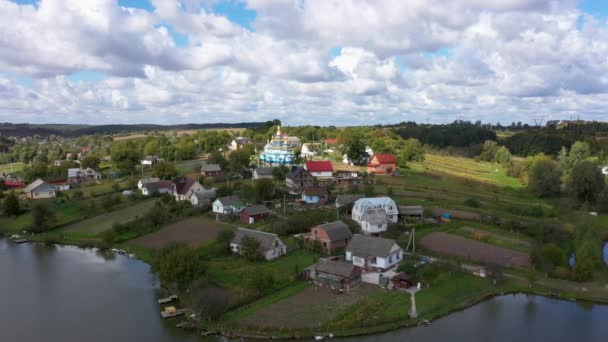 Légi kilátás gyönyörű Village Tájkép egy dombon, közel a tóhoz. Kamera követés balról jobbra. — Stock videók