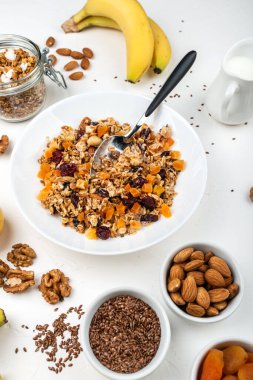 Sütlü müsli kahvaltı, kurutulmuş kayısı, kızılcık, badem ve keten tohumları beyaz arka planda. Sağlıklı kahvaltı..