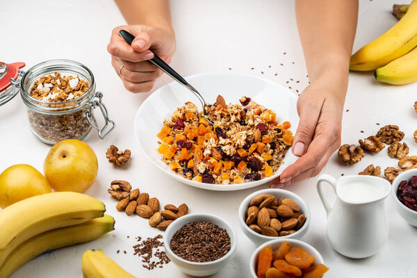 Woman eating breakfast bowl of granola muesli with milk, dried apricots, cranberries, almonds and flax seeds. Female hands hold healthy natural detox food.