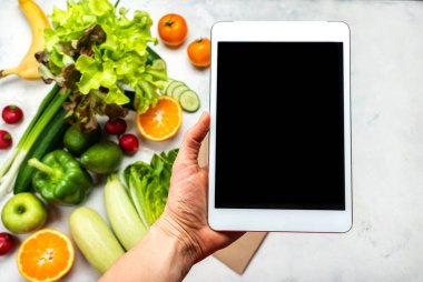 Sipariş, internete yemek teslimatı. Kadın eli tablet bilgisayarı taze sebzelerin üzerinde boş ekranla tutuyor. Yakın plan.