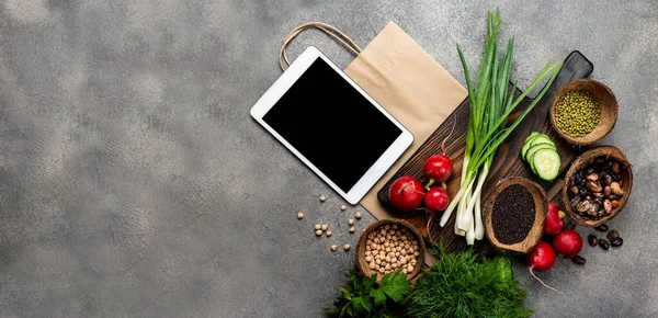 Order, delivery food. Vegetables Organic food products on a wooden board with tablet computer and shopping paper bag with copy space on the grey background. Banner