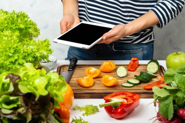 Tarifi takip eden bir kadın internette yemek pişiriyor, elinde tablet bilgisayarla mutfakta boş bir ekran tutuyor..