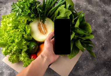 Kadın elinde akıllı telefon ve bir kutu çiftlik organik sebzesi. Sipariş Yemeği çevrimiçi konsepti.