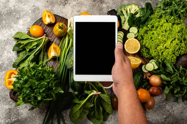 Erkek el tablet bilgisayarı taze sebzelerin üzerinde boş ekranla tutuyor.