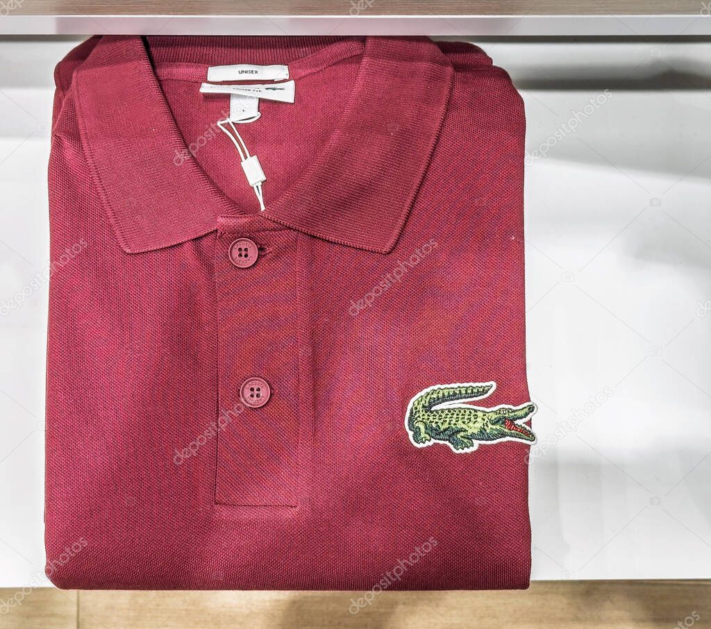 Split, Croatia - August 04, 2025: Authentic Lacoste polo in deep burgundy featuring signature embroidered crocodile emblem in retail store.