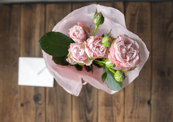 roses in a vase with envelope on wooden grey background