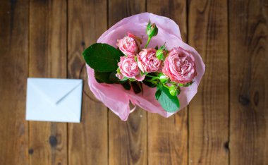 ahşap gri arka plan üzerinde zarf ile bir vazoda gül