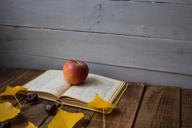 Açık kitap elma sarı kestane ahşap arka plan üzerinde bırakır.