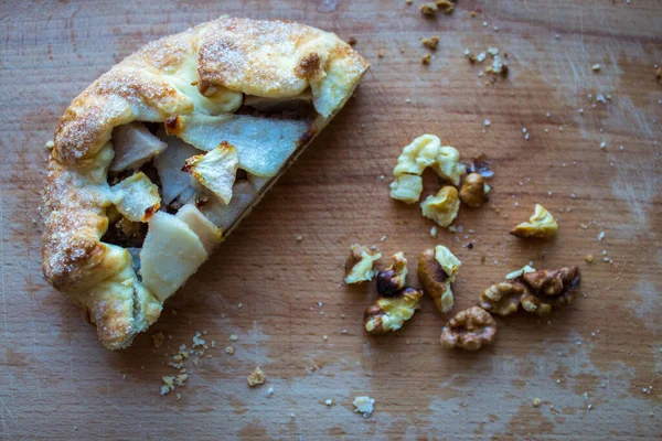 a piece of pie with pear and nuts on a wooden plank