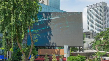 Halkla ilişkiler tabelaları dikdörtgen şekilli LED reklam tabelaları için sol köşede asılı ağaçlar var. Arkada modern bir bina var. İllüstrasyon olarak kullanılabilir. 