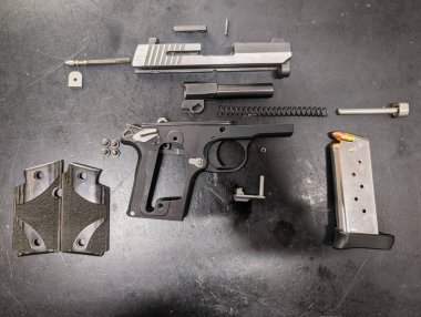 Nefsi müdafaa için sıkışık yarı otomatik tabanca tamamen parçalanmış, karmaşık iç parçalarını sergiliyor ve koyu bir yüzeyde dolu şarjörü var..