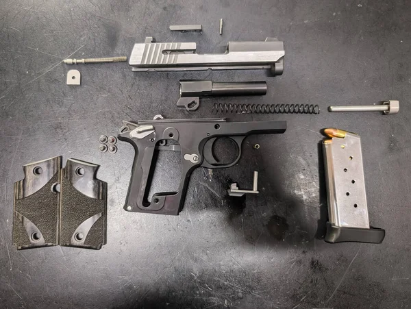 Nefsi müdafaa için sıkışık yarı otomatik tabanca tamamen parçalanmış, karmaşık iç parçalarını sergiliyor ve koyu bir yüzeyde dolu şarjörü var..