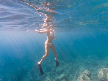 Bikini ve yüzgeçler giyen maceraperest bir kadın açık mavi Akdeniz 'de güzel güneş ışınlarında yüzüyor..