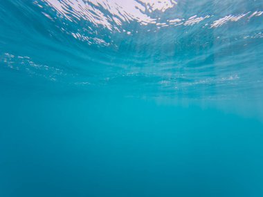 Sakin bir su altı arka planında berrak mavi su ve güneş ışığı yüzeyinde hafif dalgalanmalar var..