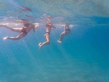 Güneşli bir yaz tatilinde açık mavi denizde yüzen bikinili üç genç kadının sualtı görüntüsü..