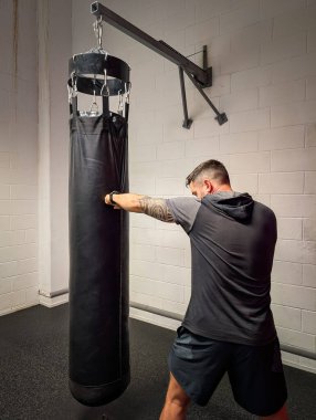 Atletizmde kolunda dövme olan kararlı bir adam idman sırasında ağır bir torbayı güçlü bir şekilde yumrukluyor. Yüksek kalite fotoğraf