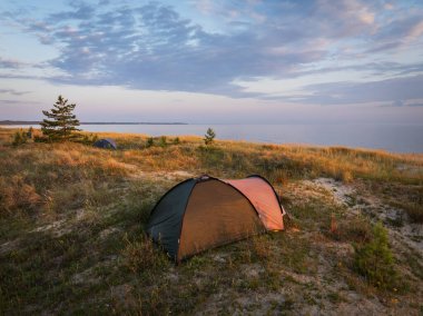 Estonya 'da günbatımında Baltık Denizi' ne bakan kumlu bir kumulda çadırları olan sakin bir kamp alanının insansız hava aracı görüntüsü.