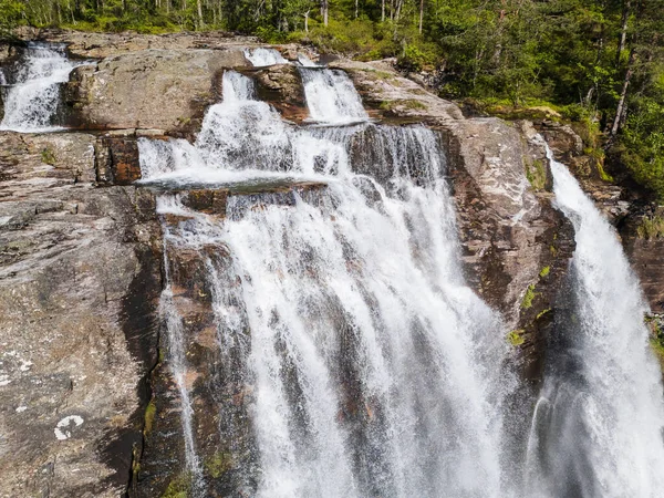 Güçlü bir şelalenin, yemyeşil bir orman çölünde engebeli kayaların üzerinde çağlayan hava aracı görüntüsü..