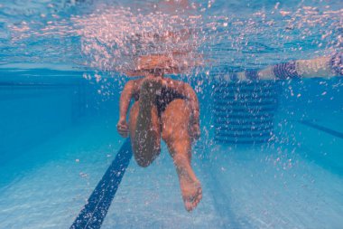 Sualtı odaklı bir havuzda yüzücü eğitimi, bacakları tekmeleme ve baloncuk bulutu yaratma..