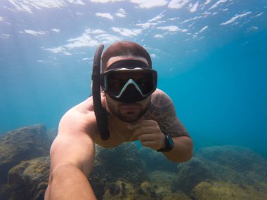 Adam, açık mavi denizde tropikal bir tatilde şnorkelle yüzerken aksiyon kamerasıyla sualtı selfie 'si çekiyor..