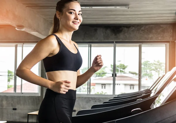 Sevimli genç kadın spor salonunda treadmill egzersiz. Koşu bandı üzerinde çalışan aktif genç kadın. gülümseme ve komik duygu.