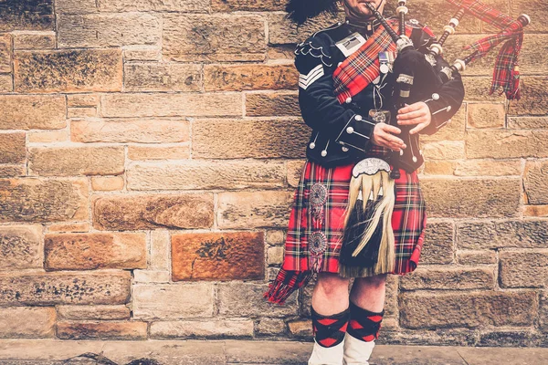 Edinburgh, İskoçya, 24 Mart 2018, İskoç gaydacı taş duvar önce geleneksel kırmızı ve siyah ekose elbise stand giymiş. Edinburgh, İskoçya'da en popüler şehir turizm.
