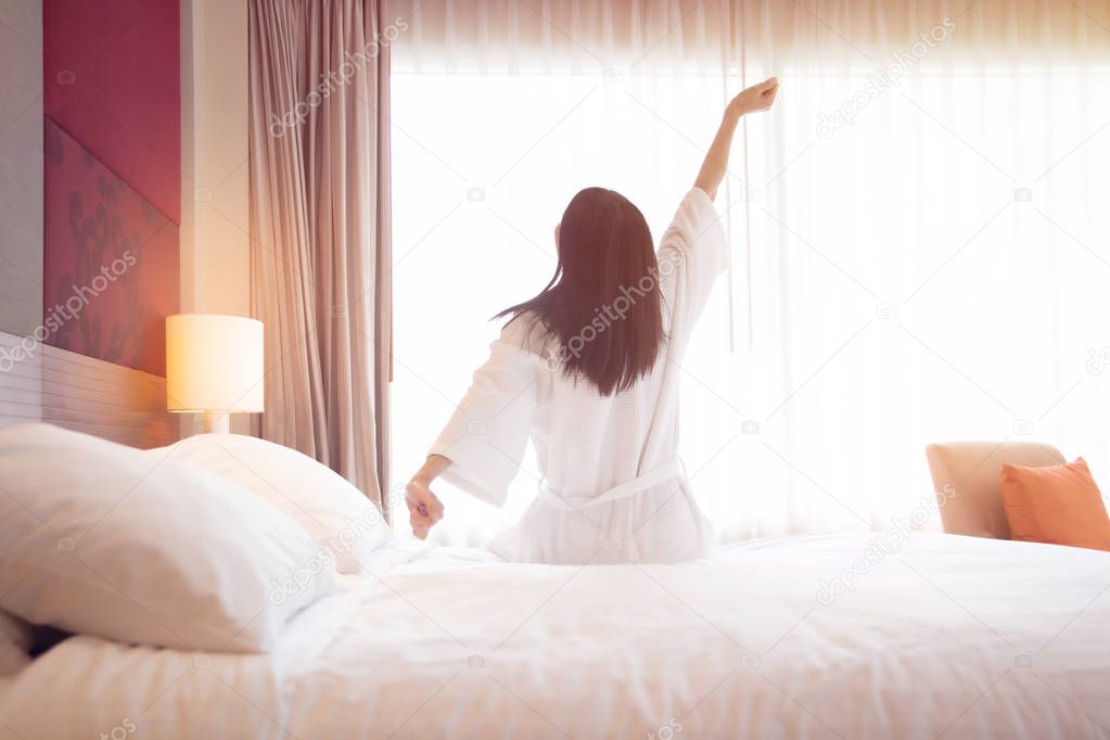 Woman stretching in bed after waking up, back view. Woman sittin
