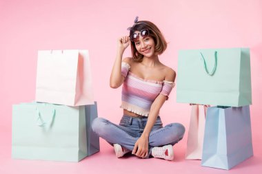Pembe pastel arka plan üzerinde oturan Asyalı güzel genç kadın. Seh