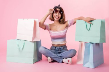 Pembe pastel arka plan üzerinde oturan Asyalı güzel genç kadın. Seh