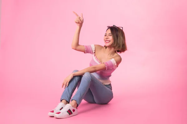 Thinking asian woman sitting on floor isolated on pink colour ba