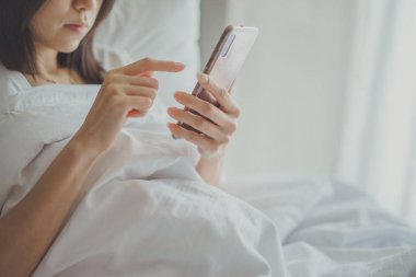 Cep telefonu ile yatakta yatak odasında Asya kız. Closeup 