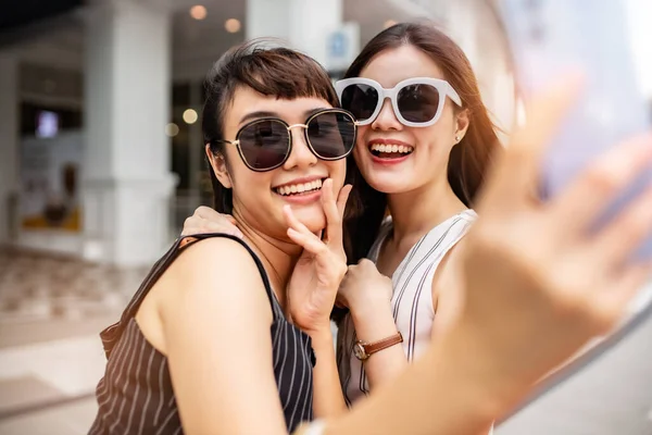 Attractive beautiful asian friends women using a smartphone.  Happy woman with shopping bags .urban city while taking self portraits with friends together with a smartphone.Girl  holding colour paper bag.Friends walking in shopping mall.