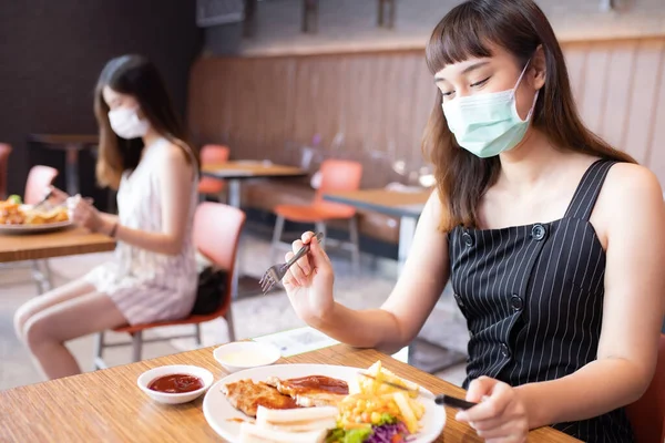 Asian woman sitting separated in restaurant eating food .keep social distance for protect infection from coronavirus covid-19, restaurant and social distancing concept.