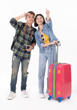 Sırt çantalı ve valizli gezgin Asyalı çift beyaz arka planda izole bir şekilde duruyor. Bir çift Asyalı yaz tatiline çıkıyor. İnsanlar, aktif yaşam tarzı, rahatlama ve neşe kavramı. Mutlu çift seyahat etmeye hazır, valizlerinin üzerinde oturuyor.